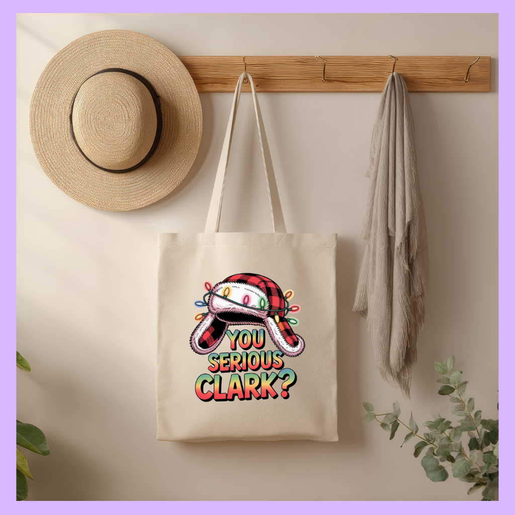 Tote bag with Christmas-themed design hanging on a wall with a hat and towel.