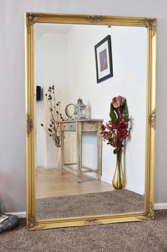 A grand gold-framed mirror rests elegantly on the floor, showcasing the Kingsbury Gold Classic Large Wall Mirror, measuring 168 x 107 cm.